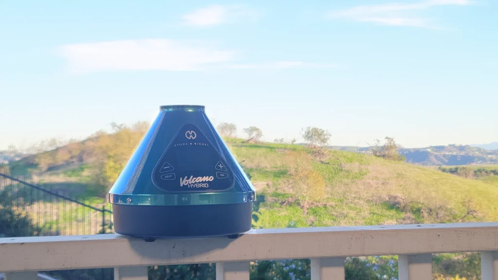 Green Volcano Hybrid rests on the ledge with green hills and blue sky 