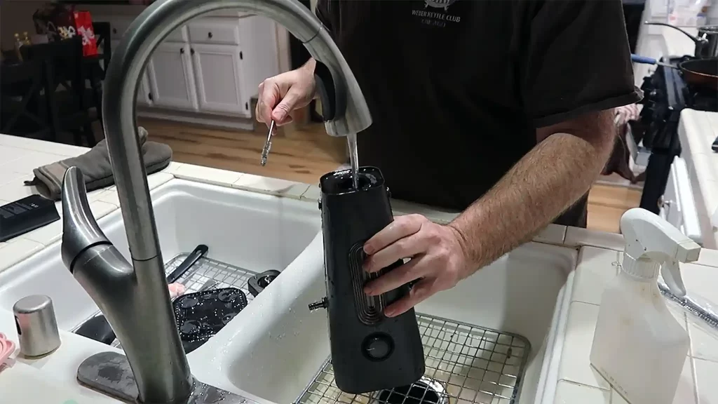 Troy carefully cleans the Enso portable hookah in the sink, with running water